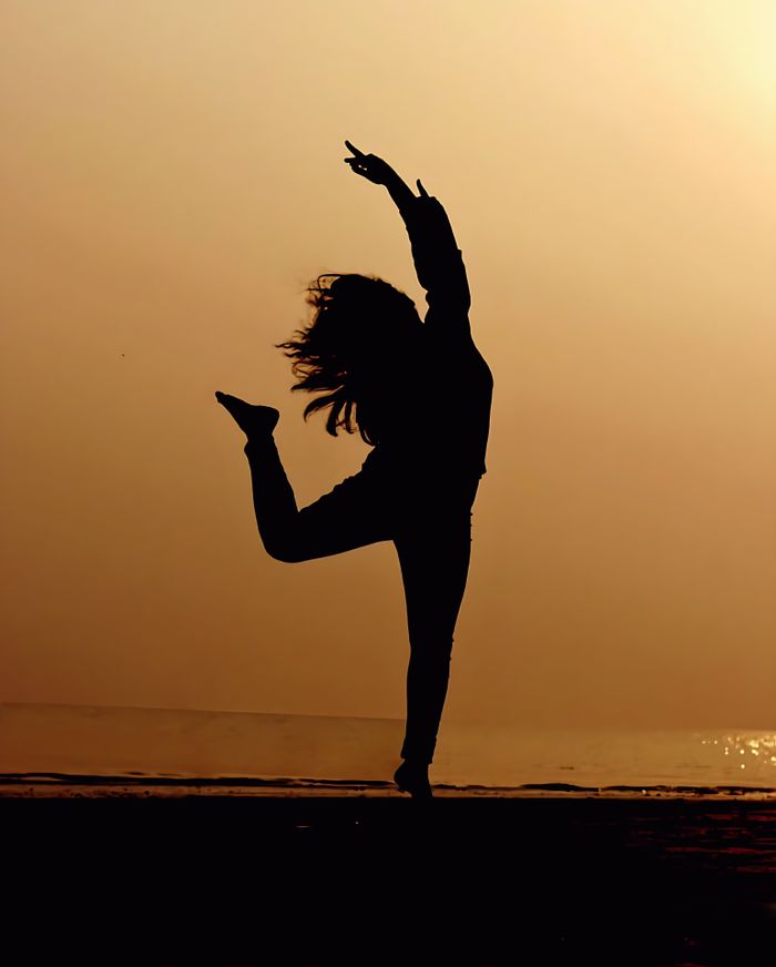 Silhouette of a dancer expressing joy against a serene sunset beach background.