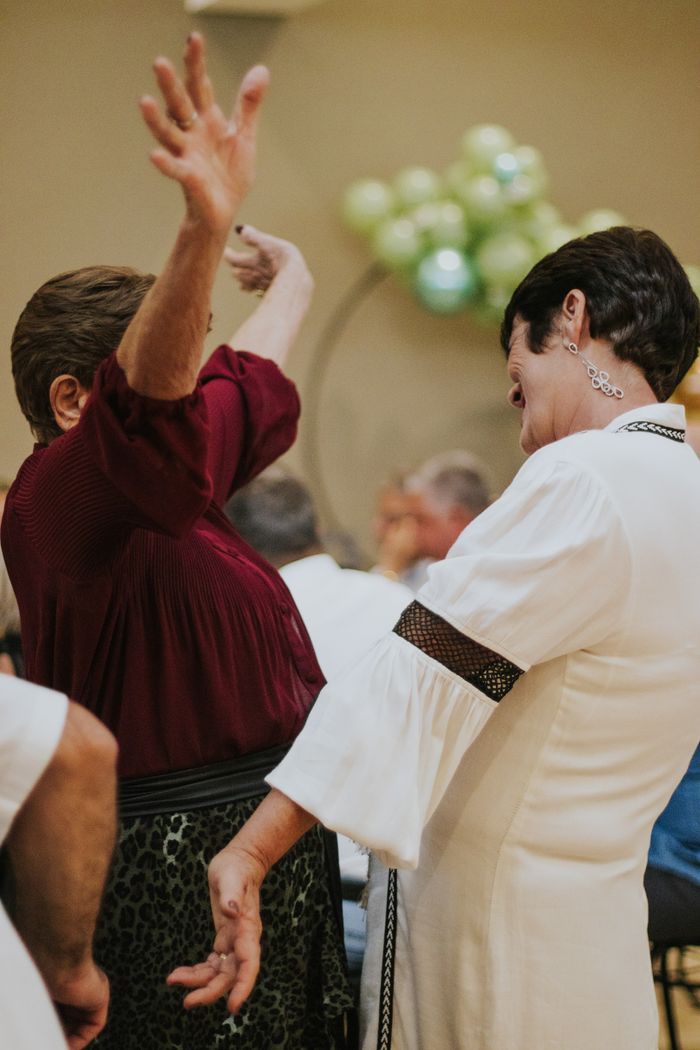 Two women joyfully dancing at an indoor celebration with balloons in the background.